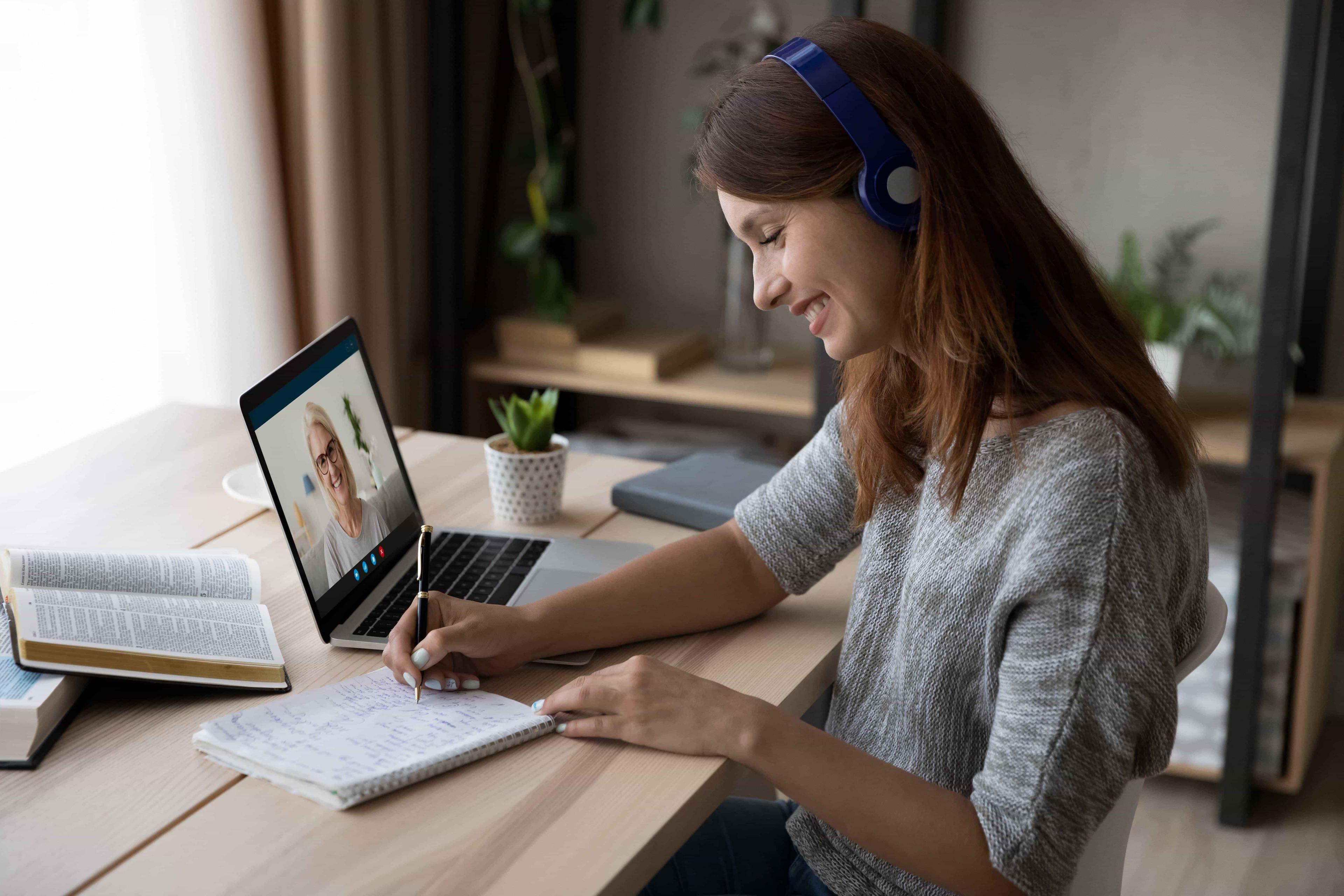 An A level student smiles at her laptop, engaging with her online tutor remotely in a virtual classroom session.