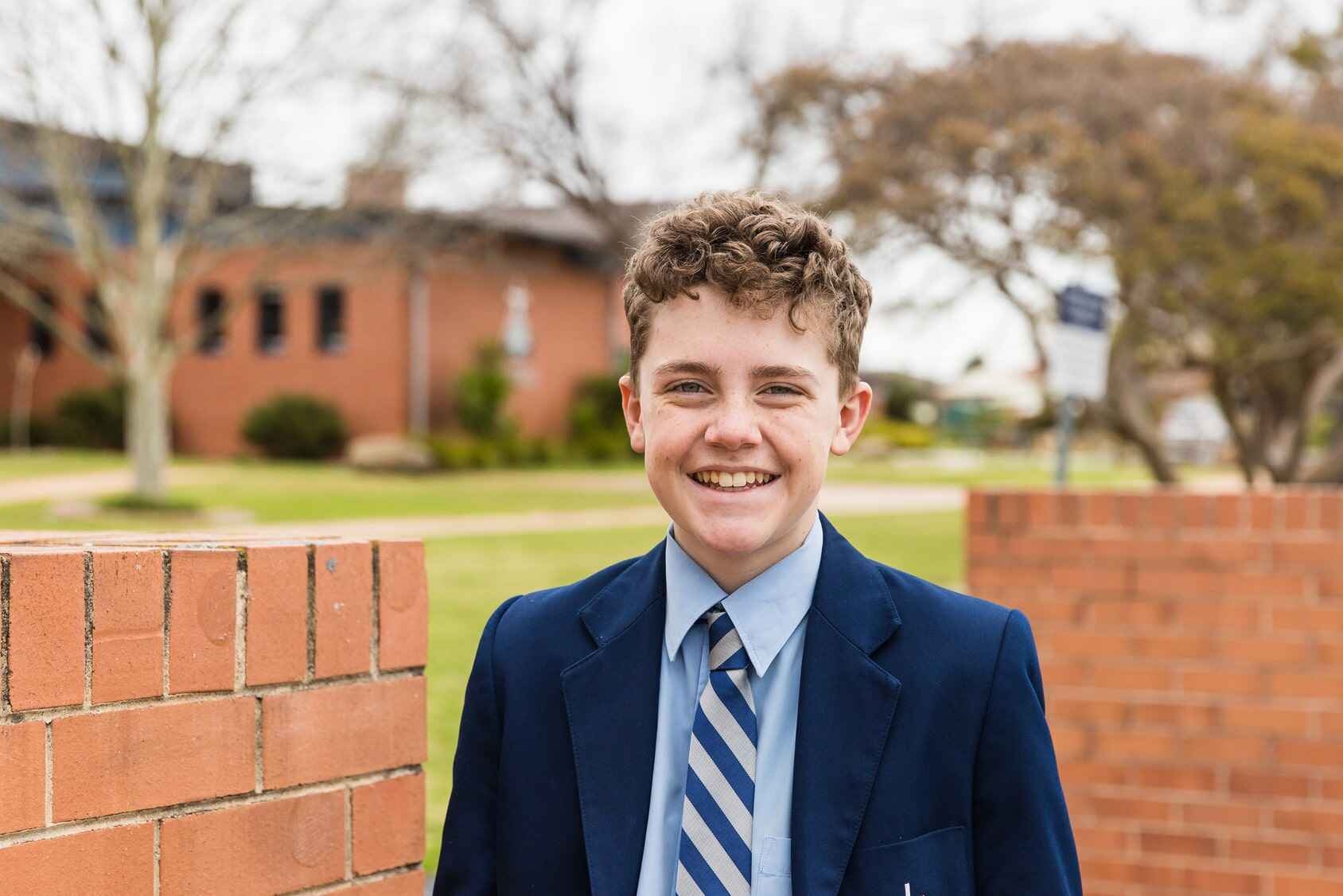 A British independent school pupil smiles in front of his school.