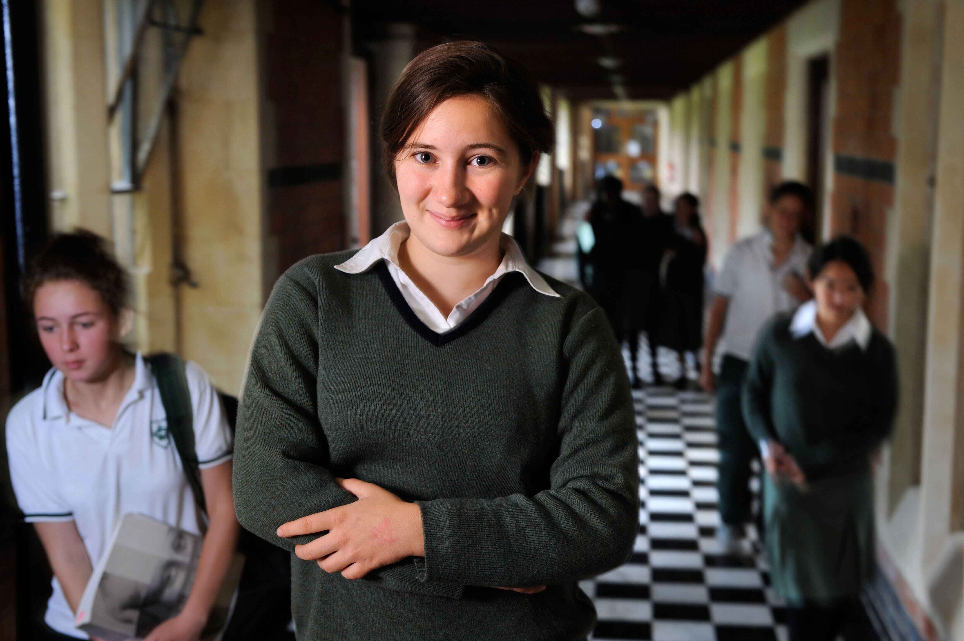 A female British private school student stands in a busy hallway in her school uniform.