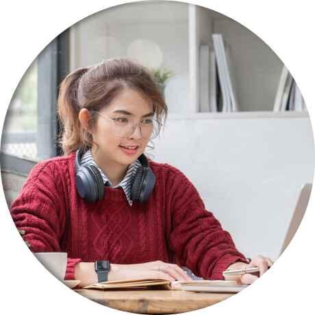 An IB student wearing headphones types on a laptop, engaging with her expert online tutor.