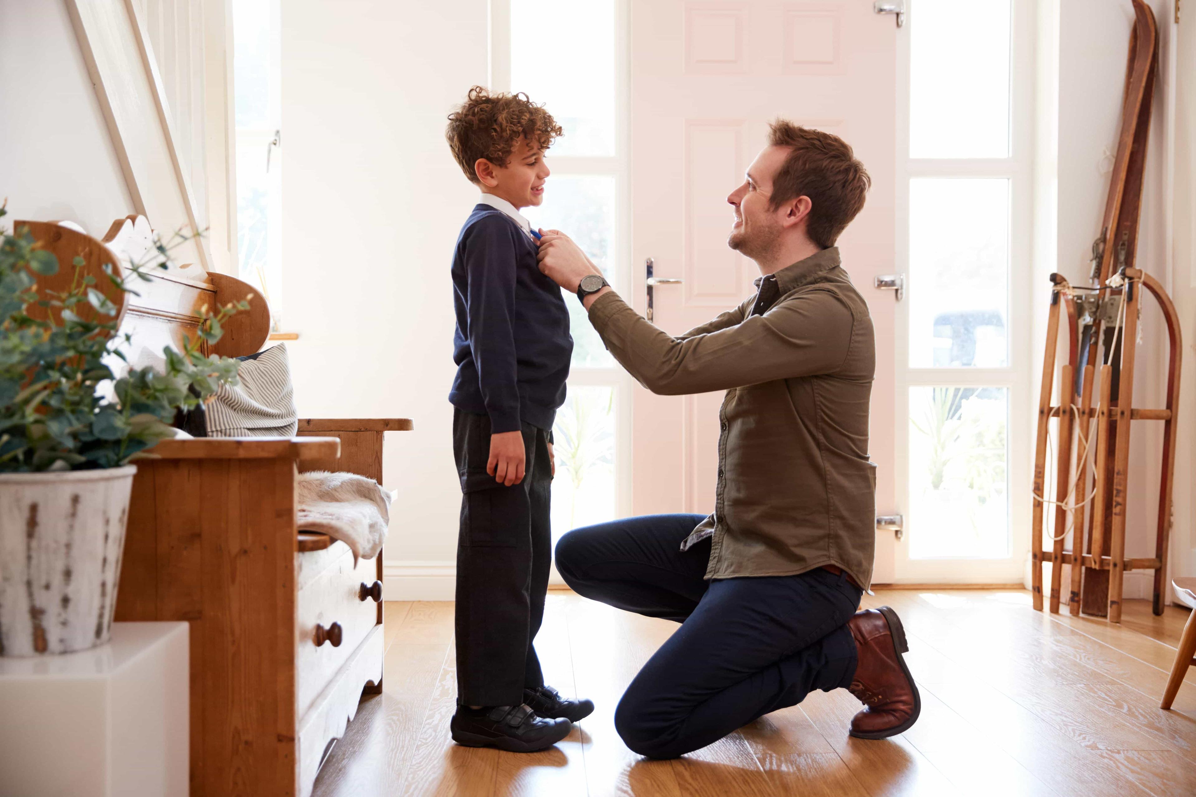 A father adjusts his son's school uniform, helping him get ready for school.